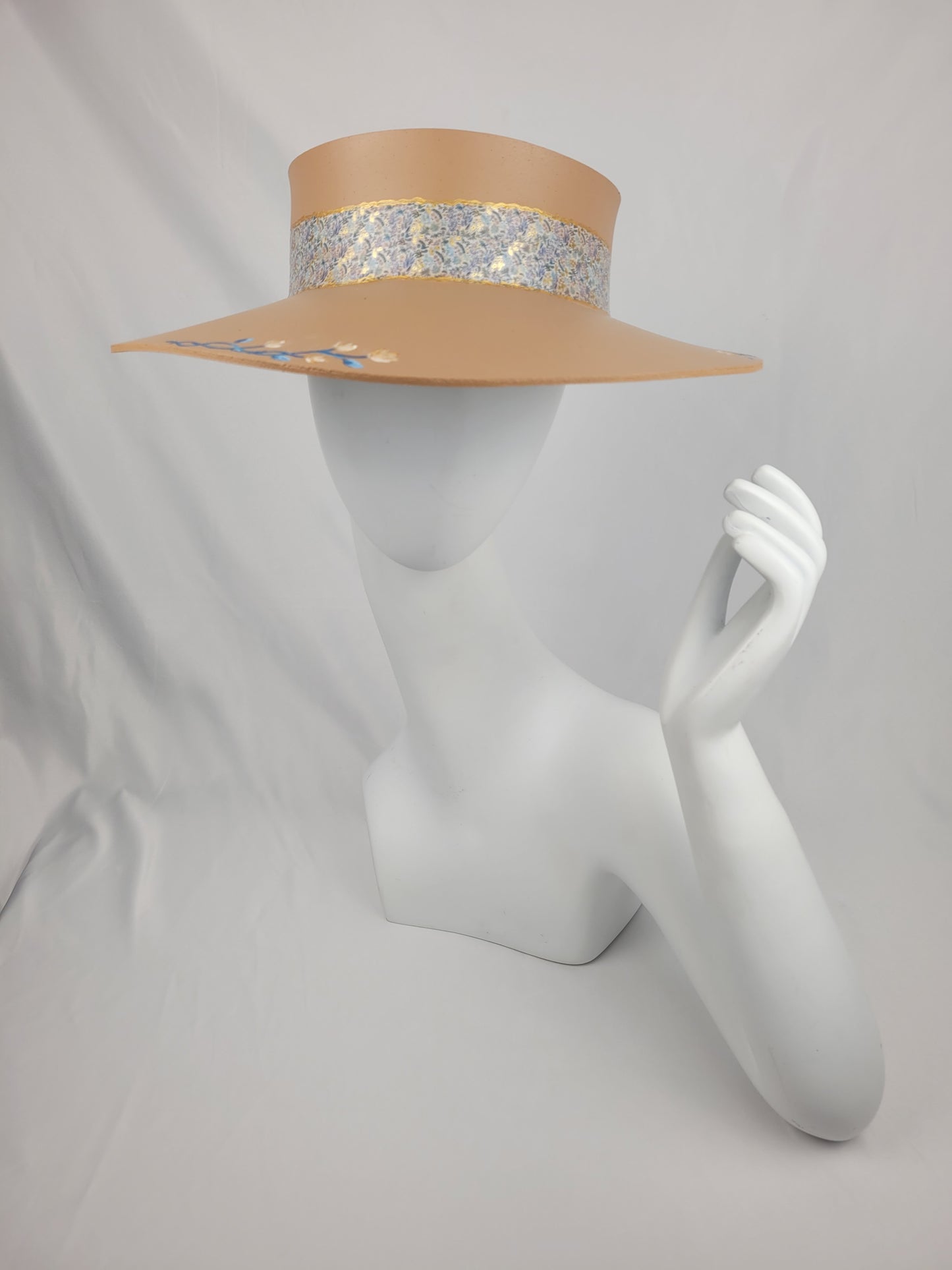 A beige visor hat with a floral band displayed on a mannequin head.