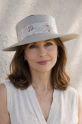 Woman wearing a light-colored hat with lace details against a neutral background
