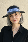 Woman wearing a black visor hat with a patterned band against a beige wall