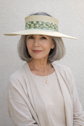 Woman wearing a wide-brimmed hat with a floral band against a plain background