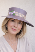 Woman wearing a lavender hat with floral decorations against a plain background