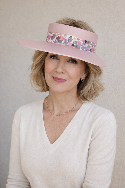 Woman wearing a pink visor with floral pattern against a plain background