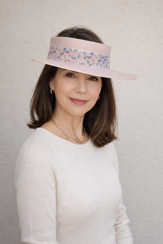 Woman wearing a light pink visor with floral band against a plain background
