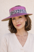 Woman wearing a wide-brimmed purple hat with floral band against a neutral background
