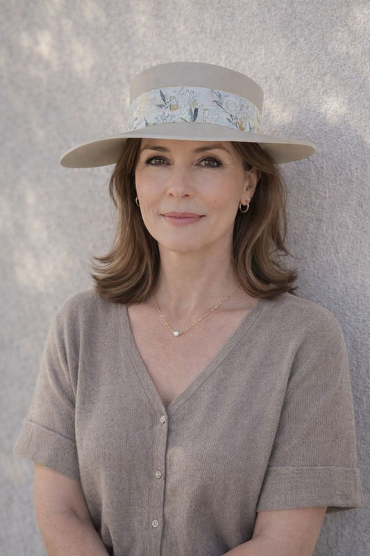 Woman wearing a wide-brimmed hat with a floral band against a gray background