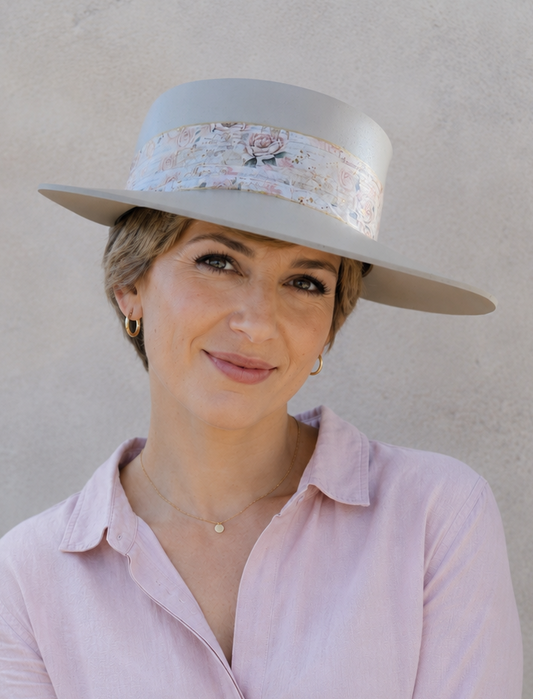 Woman wearing a light purple shirt and a wide-brimmed hat with a decorative band against a plain background
