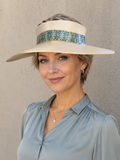 Woman wearing a wide-brimmed hat with a decorative band against a plain background