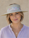 Woman wearing a light purple shirt and a wide-brimmed hat with a floral band against a beige background