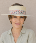 Woman wearing a wide-brimmed hat with a floral band against a plain background