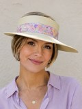 Woman wearing a light purple shirt and a wide-brimmed hat with a colorful band against a plain background