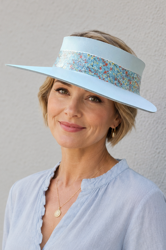 Woman wearing a light blue visor hat with floral band against a gray background