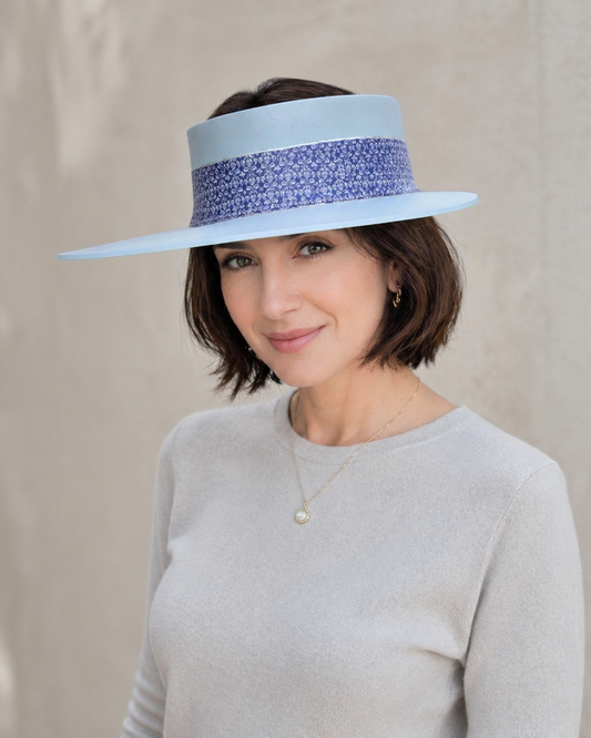 Woman wearing a light blue sun hat with a decorative band on a neutral background