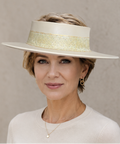 Woman wearing a white hat with a gold band against a beige background