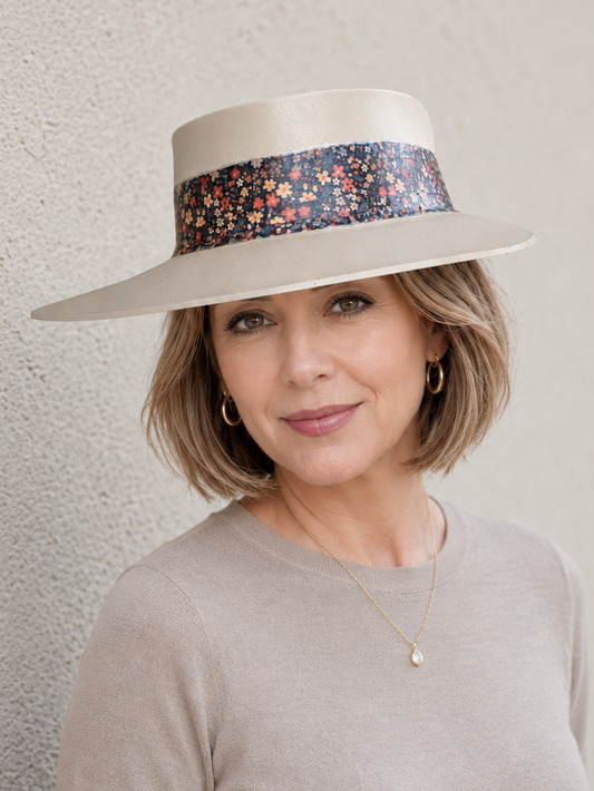 Woman wearing a wide-brimmed hat with a floral band against a neutral background