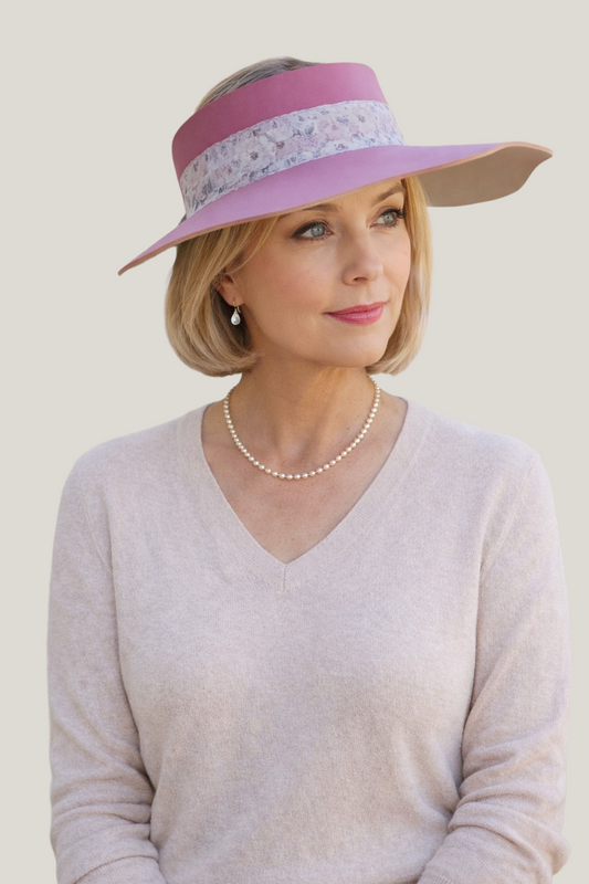 Woman wearing a pink hat with a floral band, pearl necklace, and beige sweater against a plain background