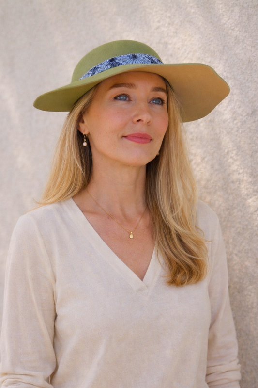 Woman wearing a wide-brimmed hat with a decorative band against a neutral background