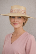 Woman wearing a beige hat with floral band against a plain background