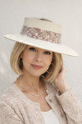 Woman wearing a wide-brimmed hat with decorative band against a plain background