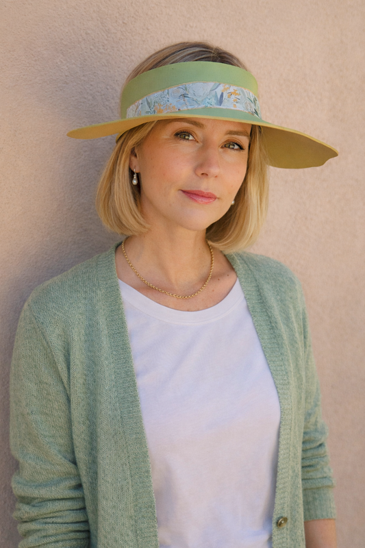Woman wearing a green visor and light green cardigan against a beige wall
