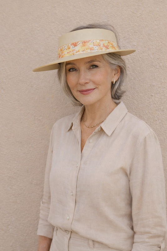 Woman wearing a beige hat with floral band against a beige wall