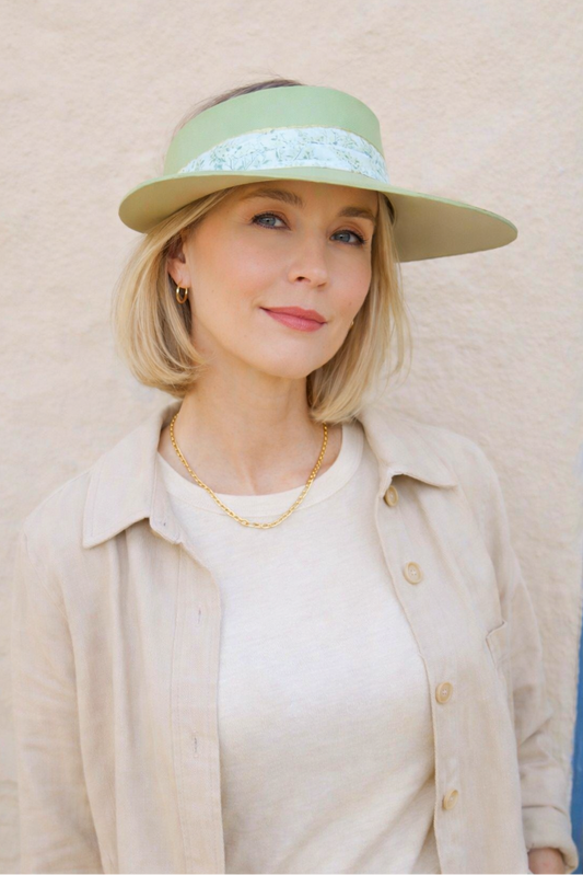 Woman wearing a light green visor hat with lace trim against a beige background