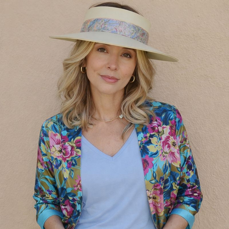 Woman wearing a colorful floral jacket and visor against a beige wall