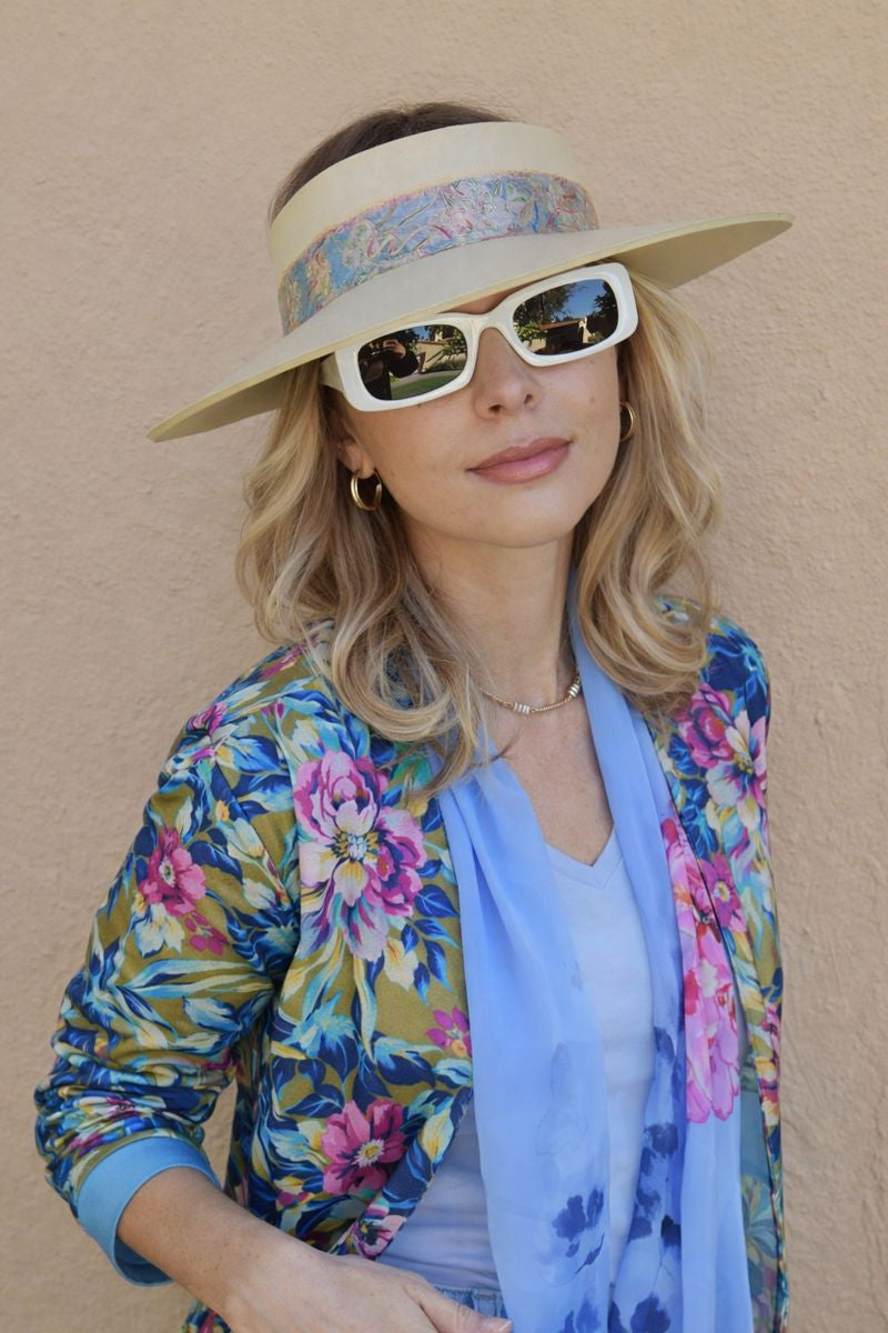 Woman wearing a floral jacket, visor, sunglasses, and scarf against a beige background