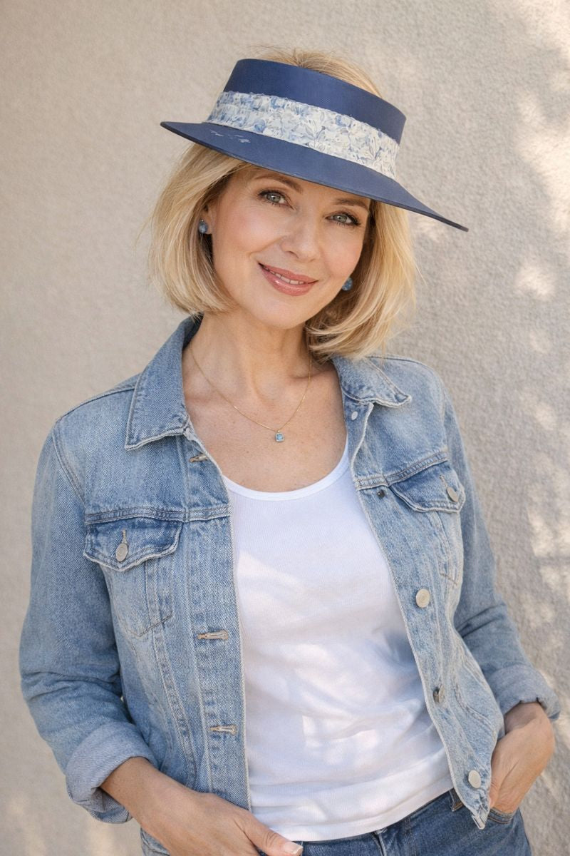 Woman wearing a denim jacket, white top, and blue hat against a neutral background