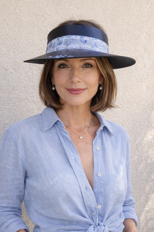 Woman wearing a blue shirt, denim shorts, and a wide-brimmed hat against a neutral background