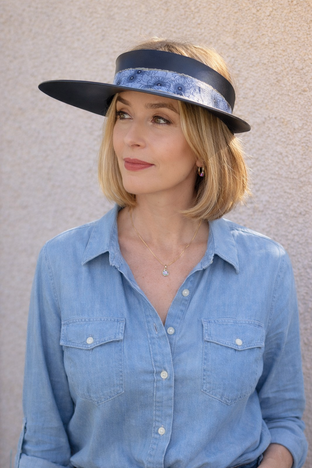 Woman wearing a blue denim shirt and a matching visor against a neutral background
