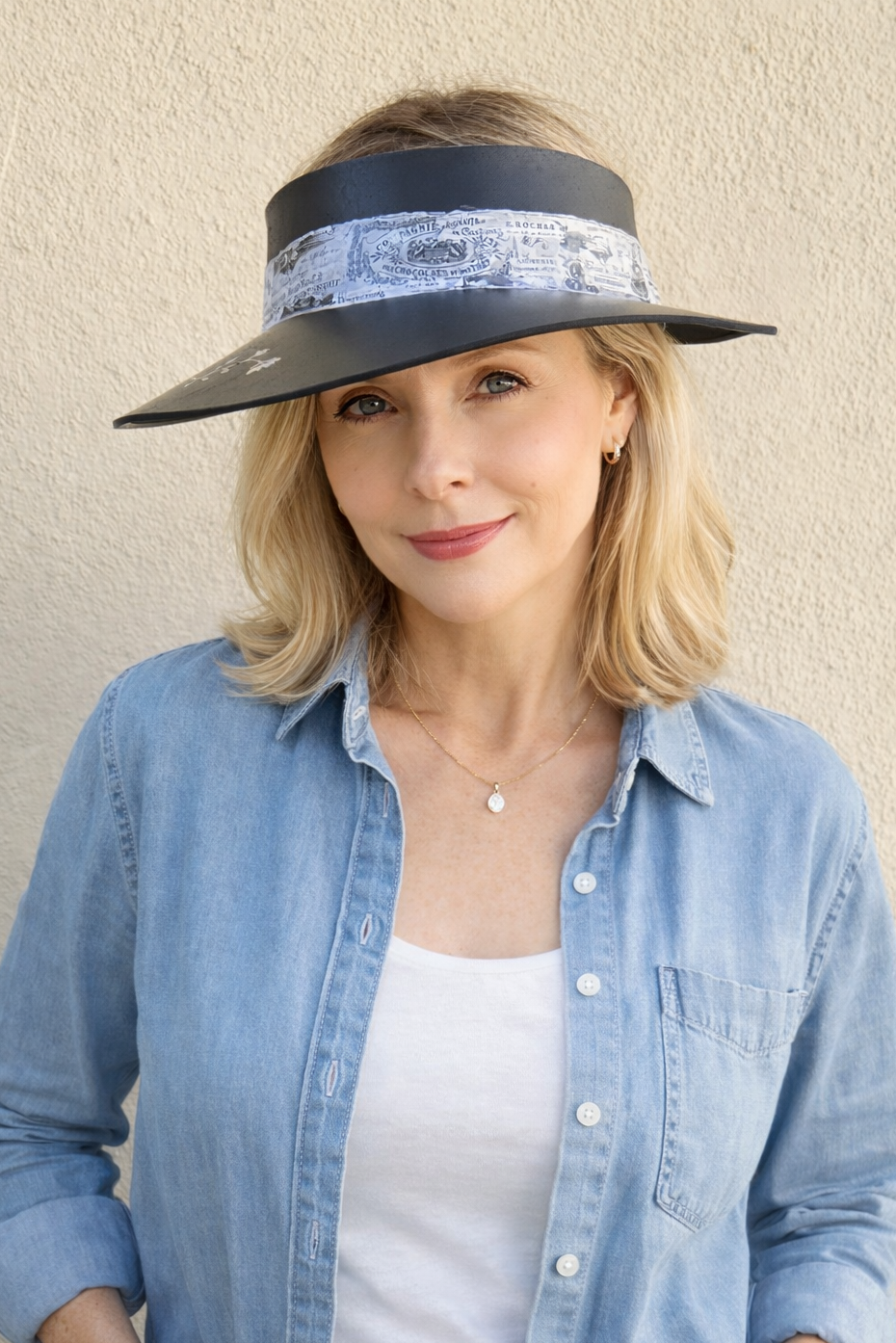Woman wearing a wide-brimmed hat with a decorative band against a beige wall.