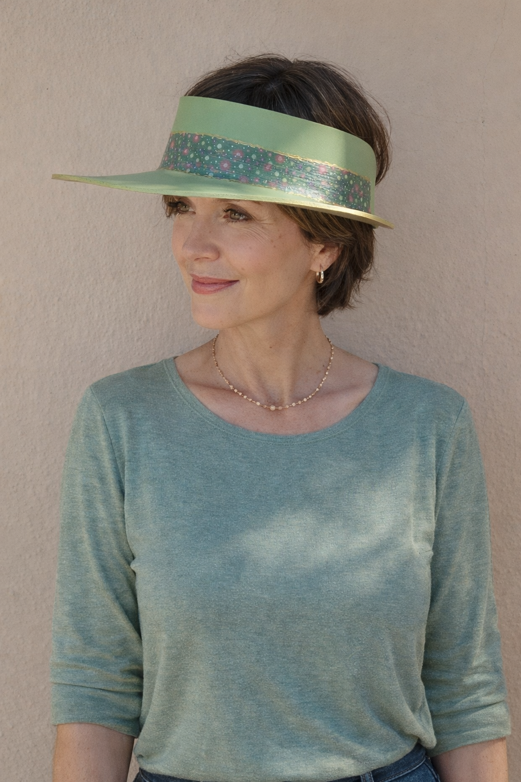 Woman wearing a green visor and matching top against a beige wall