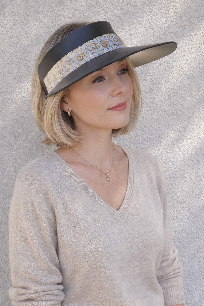 Woman wearing a beige sweater and blue jeans with a visor hat against a textured gray background
