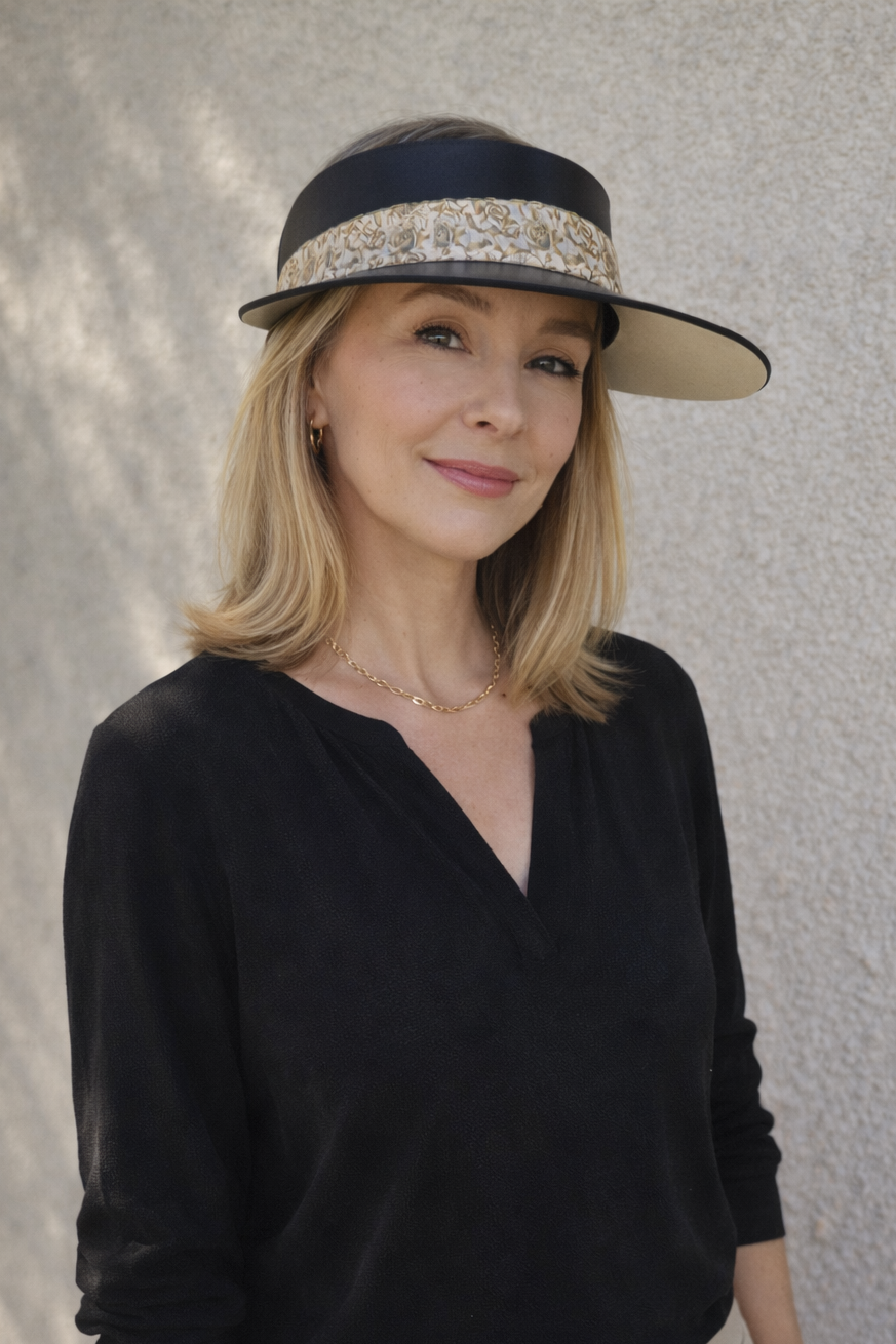 Woman wearing a black top and beige pants with a decorative visor hat against a neutral background