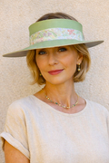 Woman wearing a light-colored dress and a green visor with floral band against a beige background