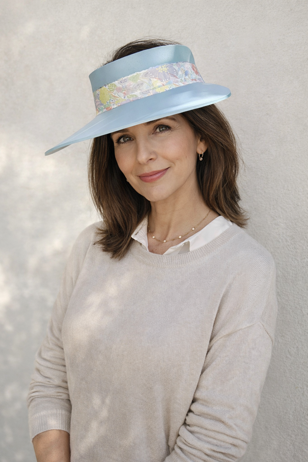 Woman wearing a light blue visor hat with floral band against a neutral background