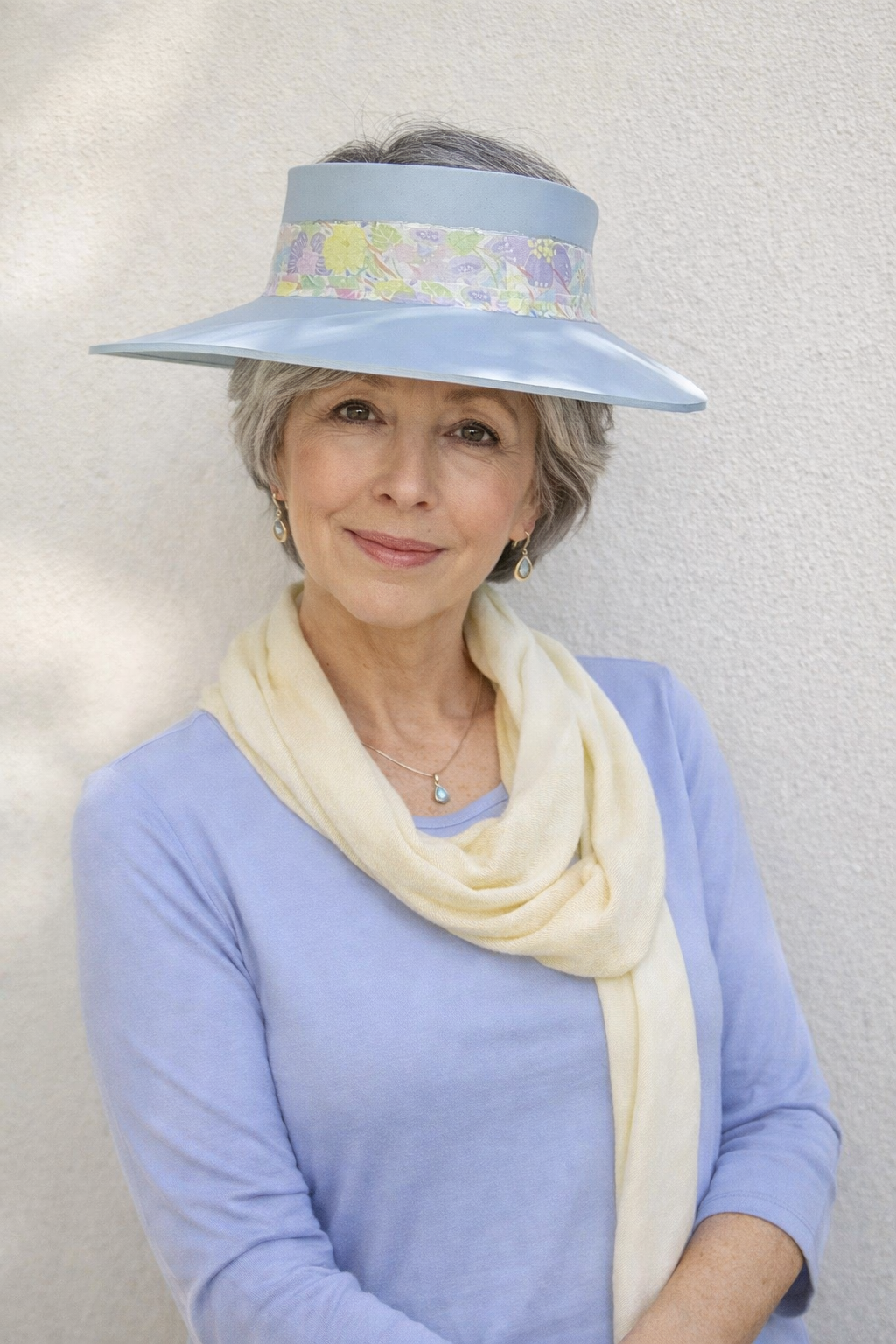 Woman wearing a light blue visor hat with floral patterns and a beige scarf against a plain background