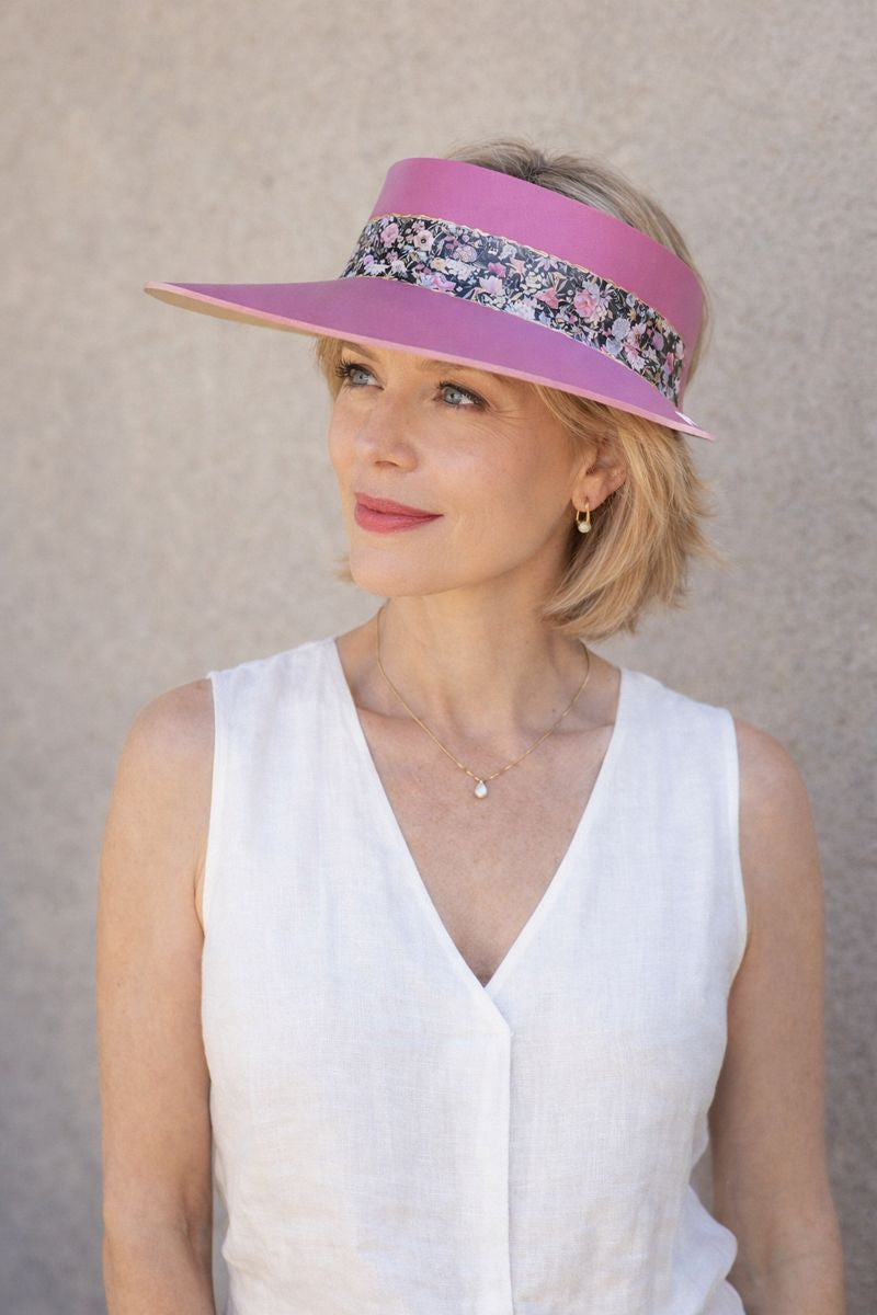 Woman wearing a pink visor with floral band against a neutral background