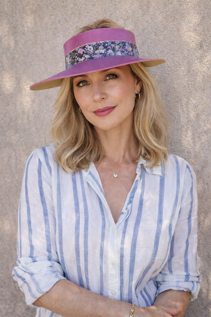 Woman wearing a wide-brimmed hat with floral band against a textured wall.