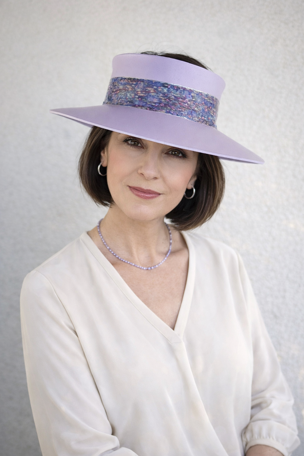 Woman wearing a wide-brimmed lavender hat with a patterned band against a plain background