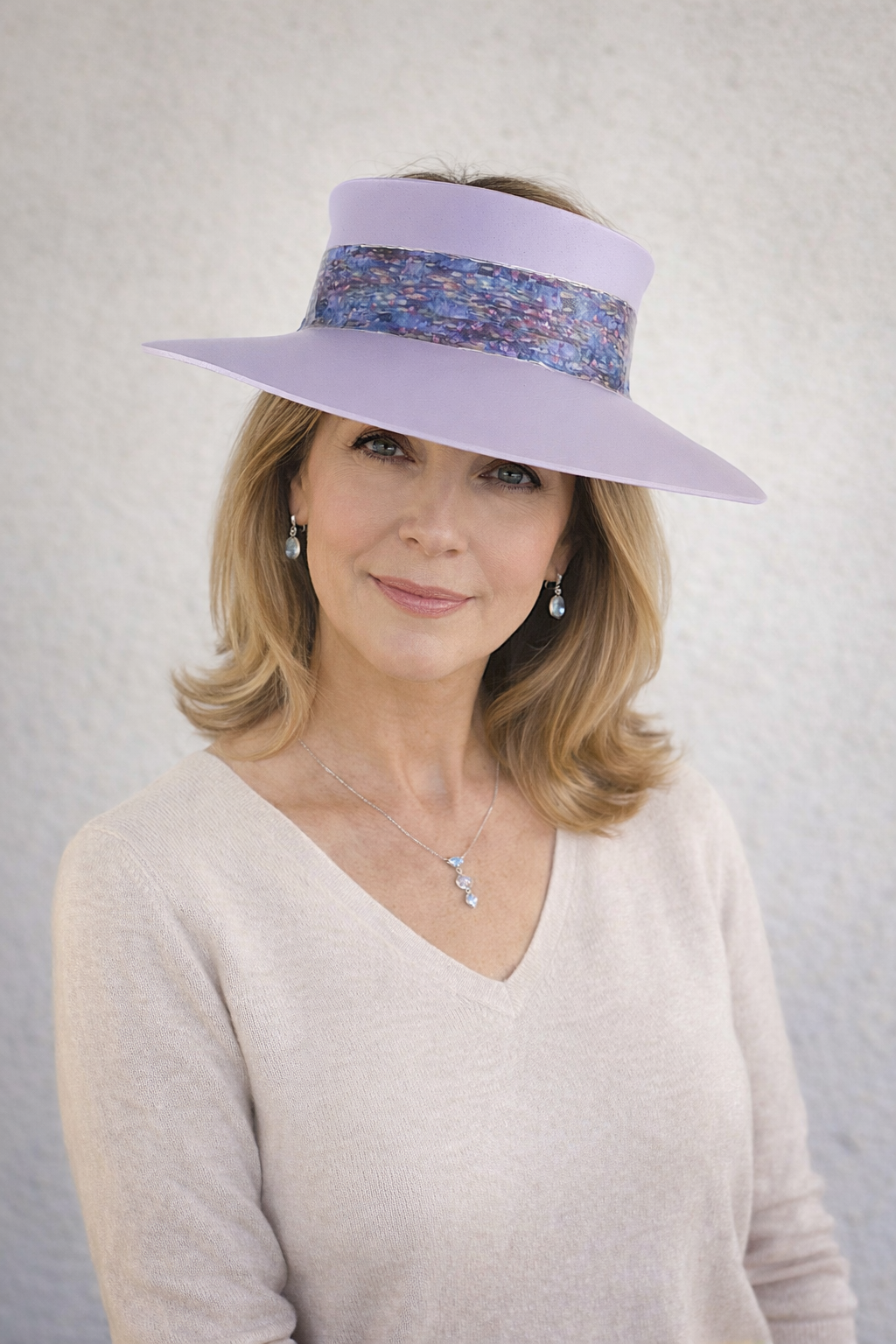 Woman wearing a wide-brimmed lavender hat with a patterned band against a plain background