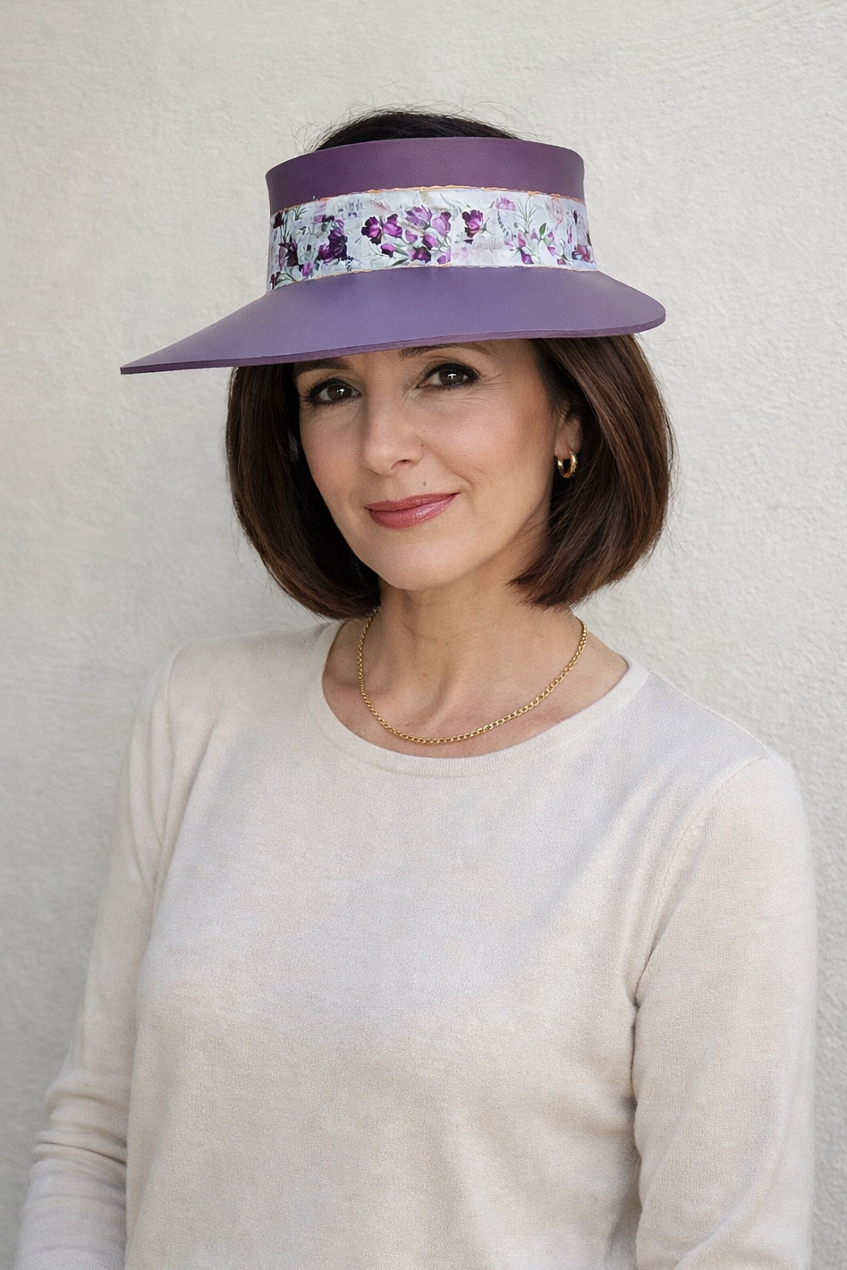 Woman wearing a purple sun visor with floral band against a plain background