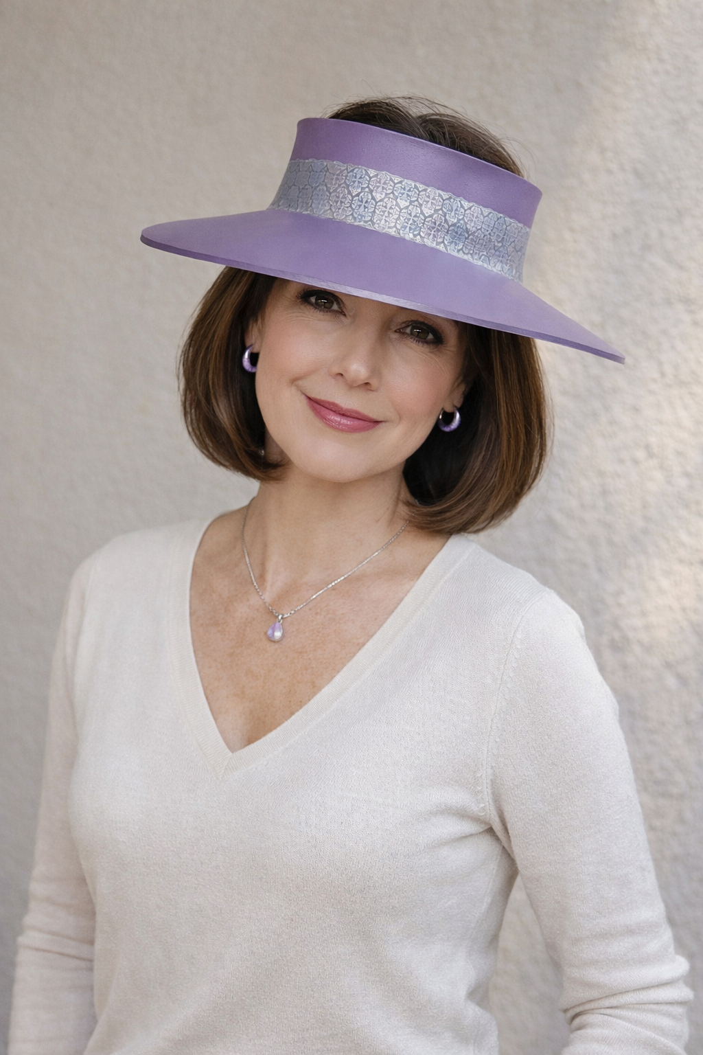 Woman wearing a wide-brimmed lavender hat with a silver band against a neutral background