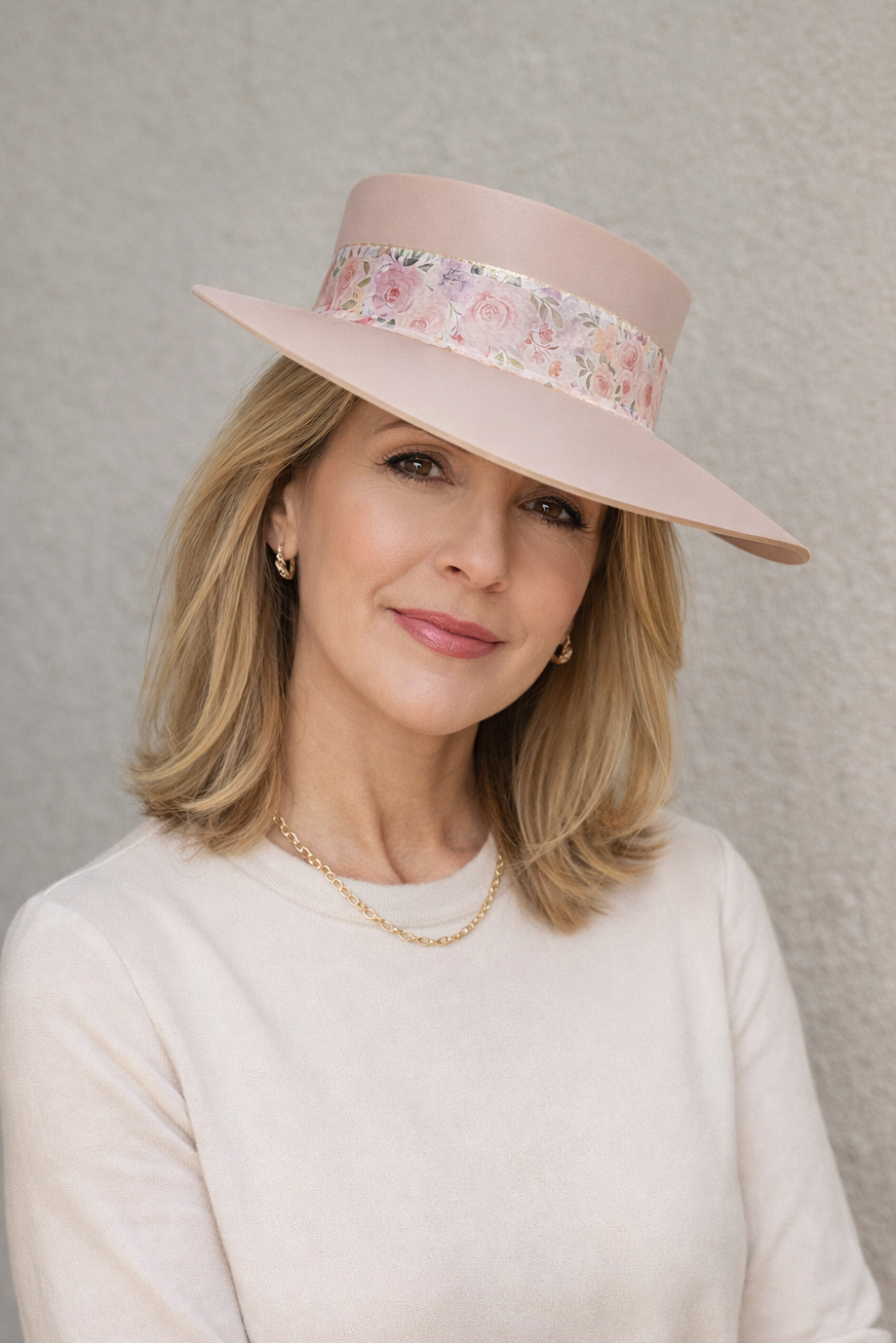 Woman wearing a pink hat with floral band against a gray background