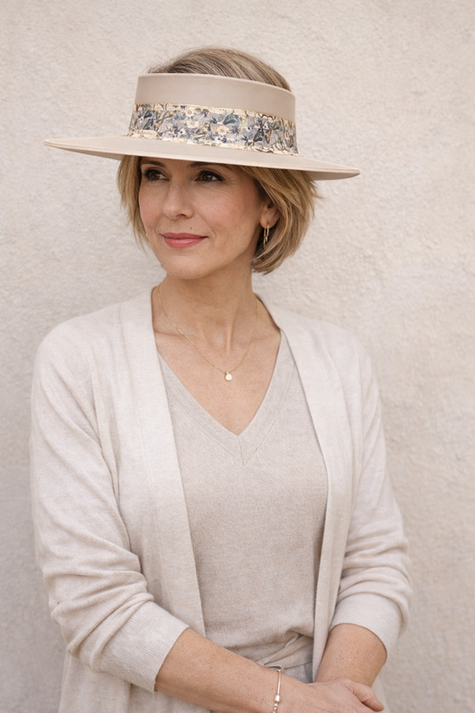 Woman wearing a beige hat with floral band against a plain background