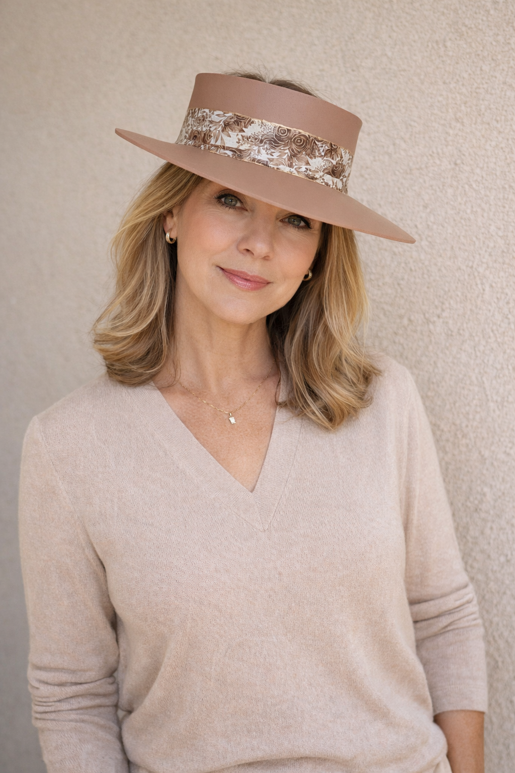 Woman wearing a beige hat with floral band against a neutral background