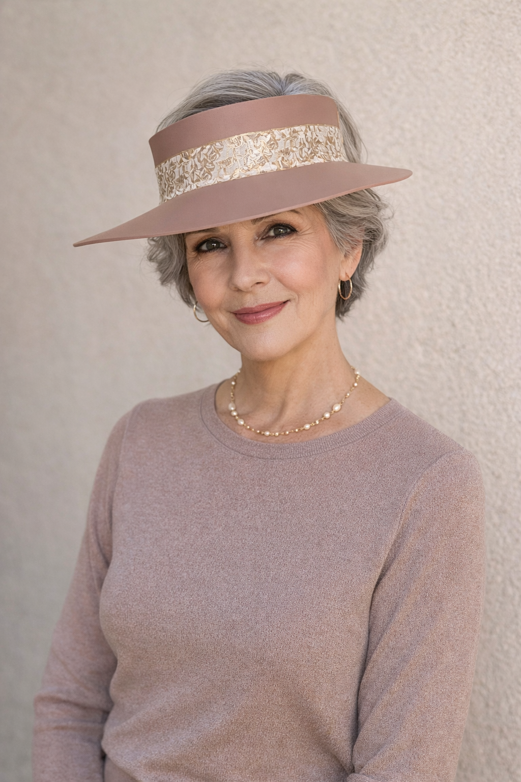 Woman wearing a pink hat with a decorative band against a plain background