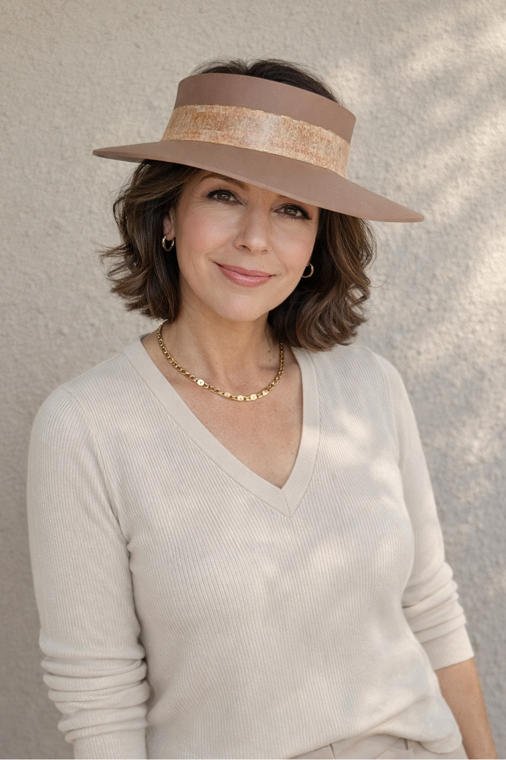 Woman wearing a beige visor hat and light sweater against a neutral background