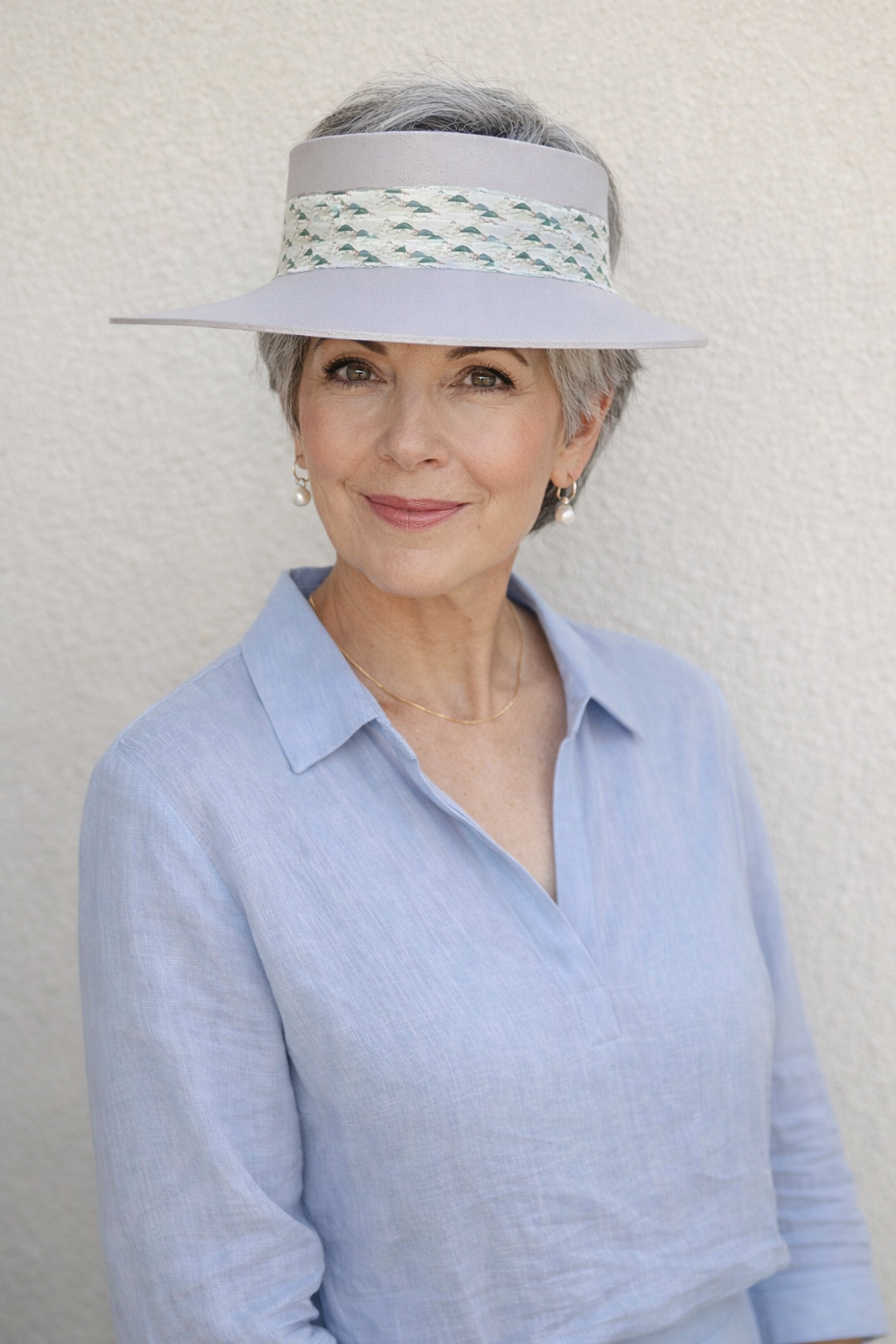 Woman wearing a light blue shirt and a visor hat against a plain background