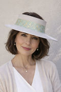 Woman wearing a white dress and beige cardigan with a decorative hat against a neutral background